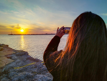 Back view woman taking photos of sunset at breakwater, Ciudad Vieja, Montevideo City, Uruguayの写真素材