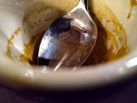 Overhead view of an empty coffee cup with a spoon resting inside. The cup has remnants of coffee stains clinging to the sides, and it sits on a saucer atop a wooden table.の写真素材