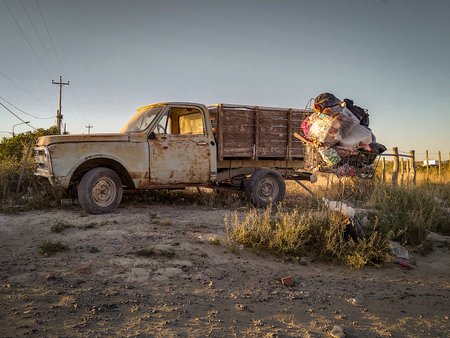 Old rusted truck overloaded with trash bags and other waste parked on a dirt path in a rural area, rio negro province, patagonia, argentinaの写真素材