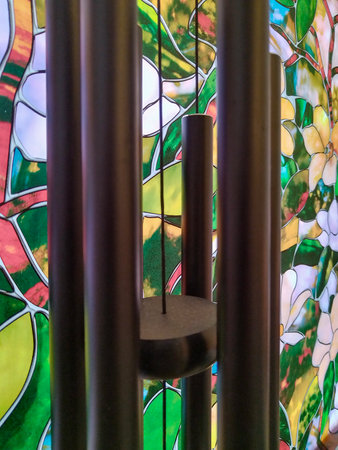 Closeup shot of  black wind chime hanging in front of a vibrant stained glass window with floral designs.の写真素材