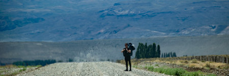 Young adult man hitchhiking at dirt road at patagonia landscape, languineo department,  chubut province, patagonia, argentinaの写真素材