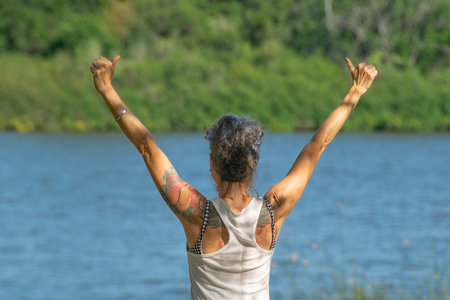 Los cerrillos, Uruguay; November 16 2024: Adult woman practicing kundalini yoga at border of river,...