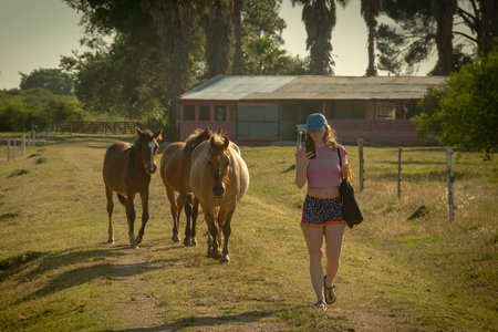 Young blonde woman followed by three horses walking at rural environent, los cerrillos, canelones department, uruguayの写真素材