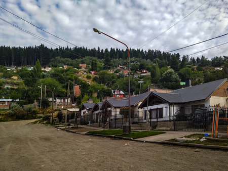 Esquel city residential neighborhood with dirt road and andes forest at background, chubut province, argentinaの写真素材