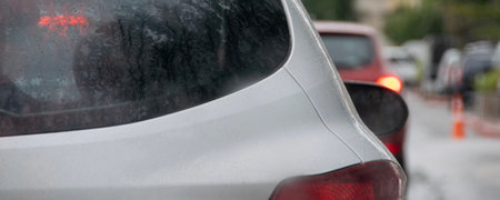 A close-up of a white car in traffic on a rainy day. The rear window is wet with raindrops, and the brake lights are on.の写真素材
