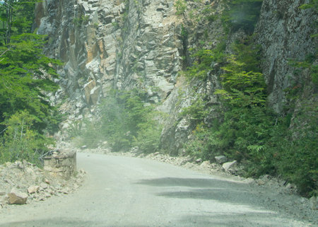 Dirt road surrouned by rocky mountain and trees at los alerces national park, a world heritage site located in chubut province, patagonia, argentinaの写真素材