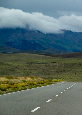 Modern highway crossing steppe patagonia andes landscape with mountains cover by clouds at background, gualjaina, chubut province, argentinaの写真素材