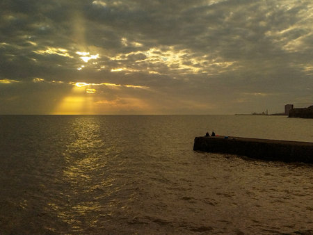 Wide shot of sun rays piercing through clouds over calm sea waters. Captured from a slightly low...