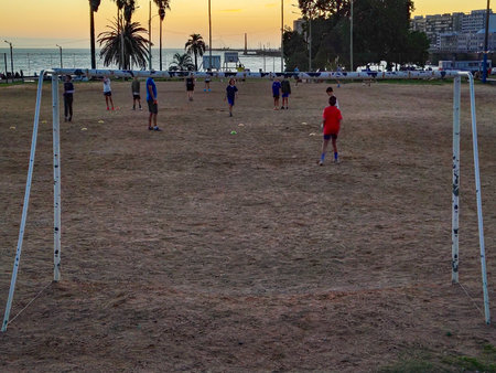 Montevideo, Uruguay: March 26 2025: A group of children playing soccer at dusk on a dry, brown field near the coast.の写真素材