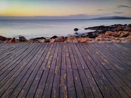 wide shot of wooden promenade in front of rocky coastal shoreline during afternoon at piriapolis city, maldonado department, uruguayの写真素材