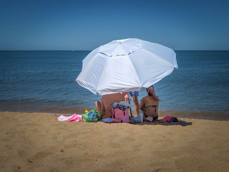 A medium, front-view shot of two people relaxing on a sandy beach under a large white parasol.の写真素材