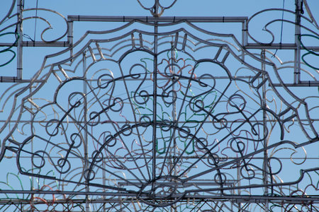 Frontal close-up of a decorative iron gate with intricate symmetrical patterns, shot against a blue sky.の写真素材