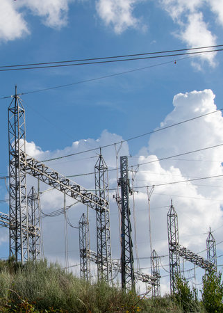 A wide, low-angle shot of a large electrical power substation situated on a green hill under a blue...