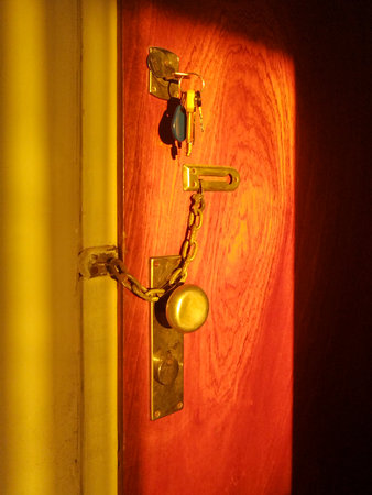 Close-up shot of a metal door handle on a warmly lit wooden door, casting a distinct shadow.の写真素材