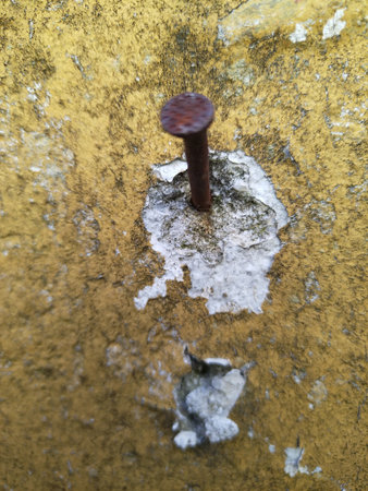Close-up vertical shot of a rusty nail stuck into an old wall with peeling paint and textured surface.の写真素材