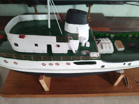 Front-facing shot of a handcrafted miniature boat model, painted white and green, placed behind a glass shelf.の写真素材