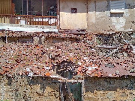 Frontal close-up view of a deteriorating structure with a collapsed tiled roof and crumbling walls, conveying abandonment and urban decayの写真素材