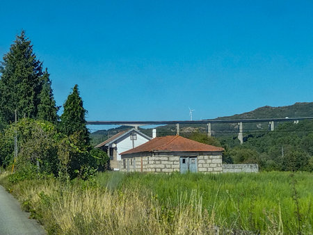 Frontal view of a quiet rural road with rustic buildings and big modern bridge at top; vila real, portugalの写真素材