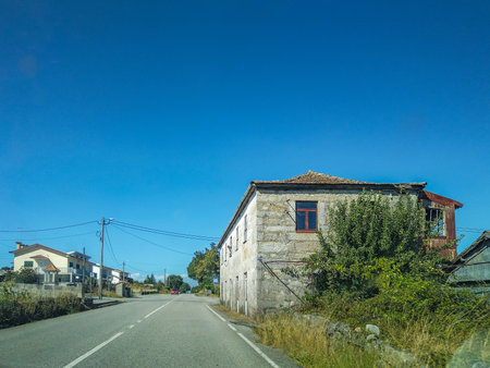 Frontal view of a quiet rural road stretching into the distance with a solitary abandoned building at the side.の写真素材