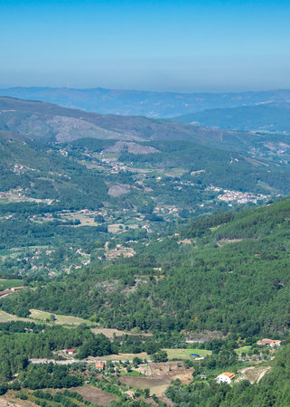 High-angle view of a vast mountain valley with dense forest, scattered houses and winding roads...
