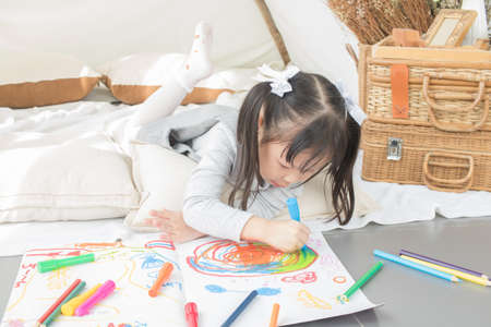 Asian little girl painting on paper in white room at homeの写真素材