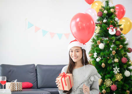 Asian beautiful woman holding gift box. Smiling face in room with decorated Christmas treeの写真素材