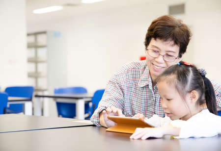 Grandmother and granddaughter playing game together with tablet at libraryの写真素材