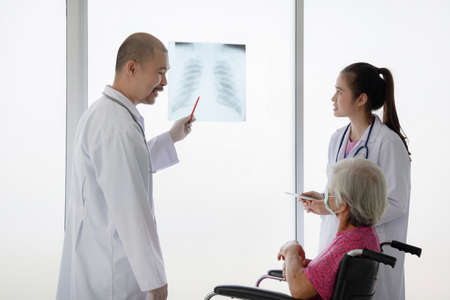 Asian doctor explain X-ray film result to his  elderly patient in hospital