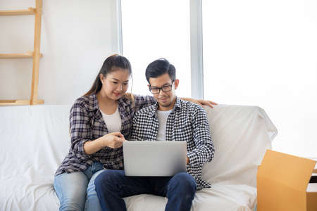 Young couple moving to a new home relaxing sitting on sofa and using laptop for shopping onlineの写真素材