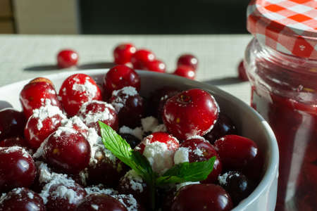 Cherries and a jar of jam on background and fresh fruits on the table, closeupの写真素材