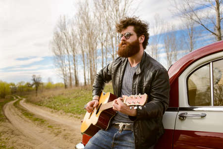 Bearded man playing guitar outdoors near retro carの写真素材