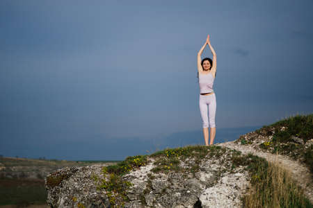 Young woman doing complex Yoga exercise on a rockの写真素材