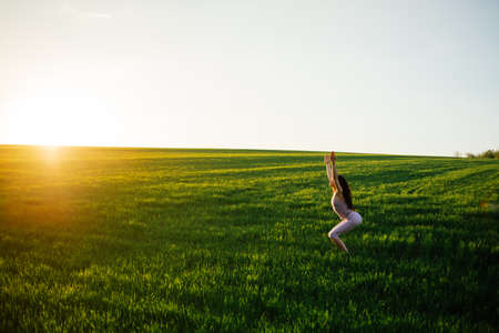 Young woman doing complex Yoga exercise on green lawn at sunsetの写真素材