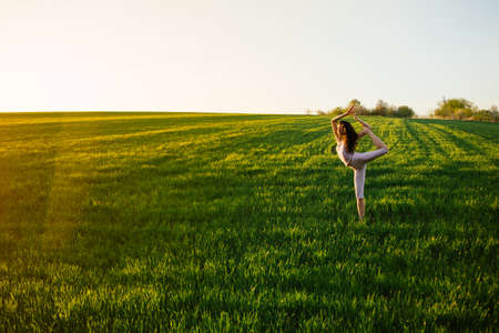Young woman doing complex Yoga exercise on green lawn at sunsetの写真素材
