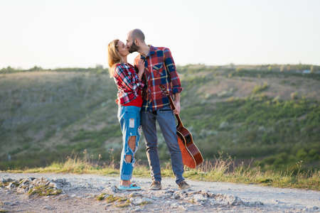 Young couple in love sitting on the park  while these young guitar playing guitar in sunset time.の写真素材