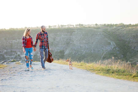 Young couple in love sitting on the park  while these young guitar playing guitar in sunset time. Together with dogsの写真素材