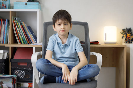 Sad little boy sitting on chair at home and looking at camera.の写真素材