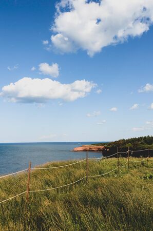 Rope fence in tall grass at the edge of the red cliffs at Prince Edward Island National Park, Canadaの写真素材