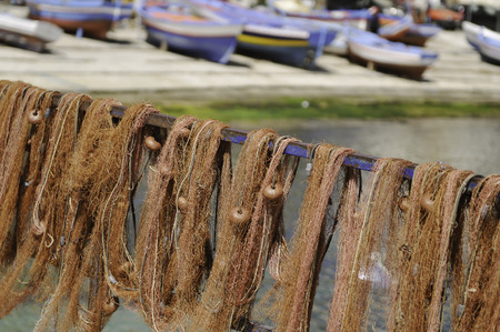 Picturesque red fishing nets hung out to dry and colorful boats at the background in the harbour of...