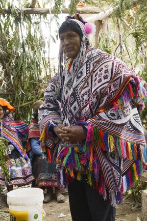 Native Peruvian man wearing a handwoven poncho and a chollo - knitted hat with earflaps, attending his daughter wedding ceremony. Next to him is a bucket with chicha - local beer derived from maize. October 22, 2012, Amaru, Peruのeditorial素材