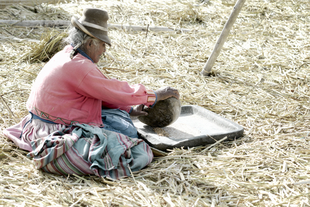 An elderly Aymara woman grinding corn, The Uros Floating Islands, Lake Titicaca, Peruのeditorial素材