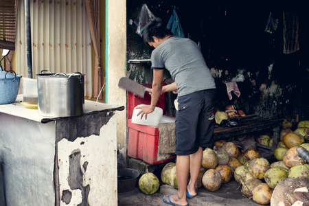 Seller cutting an ice block for the coconut drinks he offers at the Surabaya Market. January 17, 2014 - Surabaya, Java, Indonesiaのeditorial素材