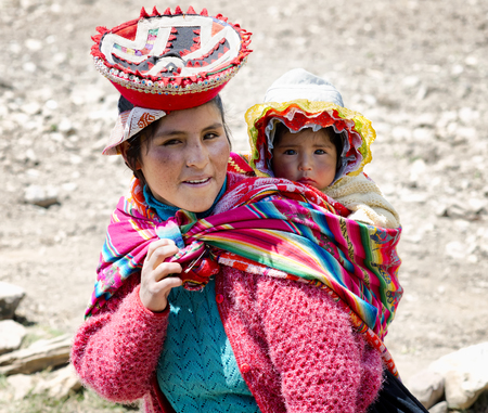 Close up of portrait of a smiling Quechua woman dressed in colourful traditional handmade outfit and carrying her baby in a sling. October 21, 2012 - Patachancha, Cuzco, Peruのeditorial素材