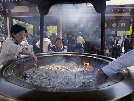 Japanese woman lights incense stick in the large bronze incense burner or koro at Senso-ji temple. April 15, 2014 - Asakusa, Tokyo, Japanのeditorial素材