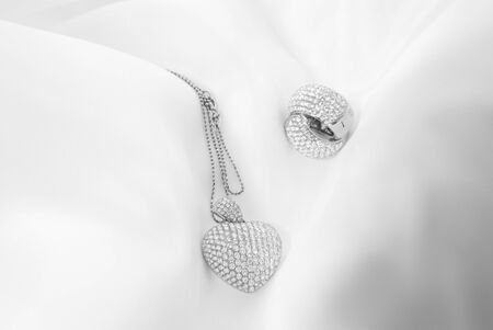White gold earrings and heart shaped necklace with white diamonds on soft blurred backgroundの写真素材