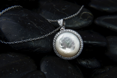 White gold pendant with Nacre and diamonds on black stones backgroundの写真素材