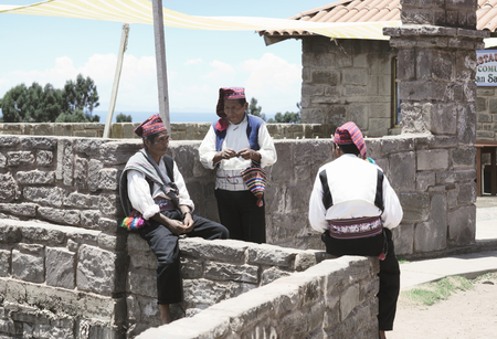 Three men dressed in traditional outfits specific for the Taquile Island region, one of them knitting a hat. Lake Titicaca, Peru - October 17, 2012のeditorial素材