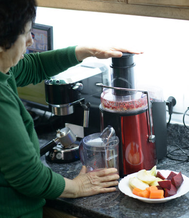 Elderly woman creates a nutritious juice blend using fresh apples, carrots, and beetrootの写真素材