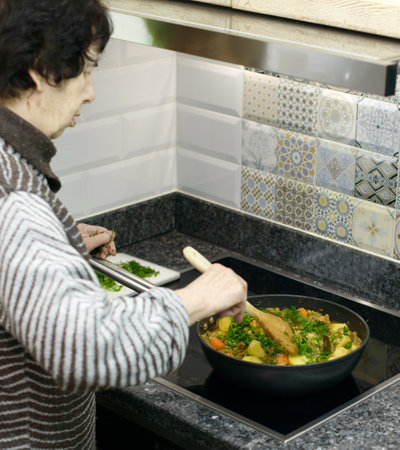 An elderly woman prepares a traditional dish of green beans, carrots, and potatoes in her kitchenの写真素材