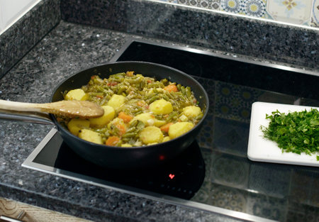 A close-up of a person stirring a homemade stew of green beans, carrots, and potatoes, and parsley on the sideの写真素材
